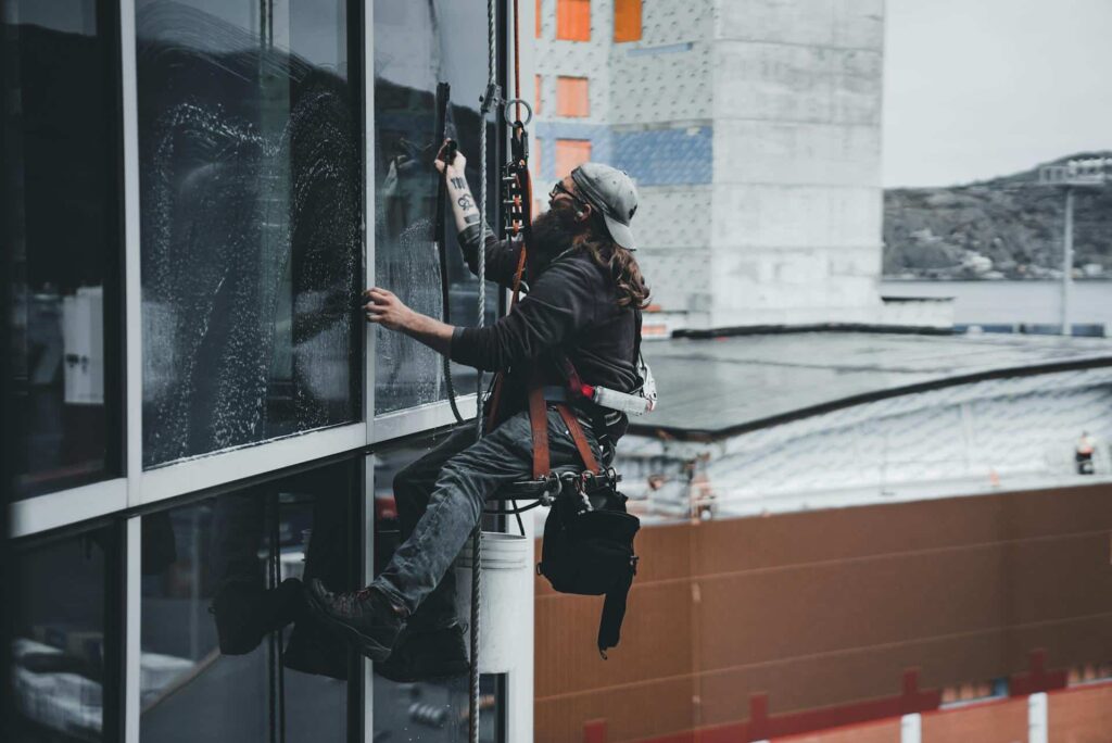 A window cleaner ascends a high-rise building, focused on cleaning the glass surfaces for a clear view.